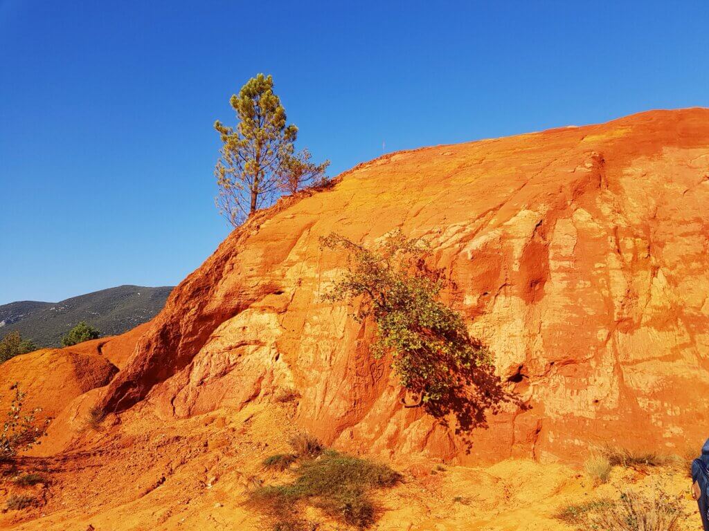 Roche orange avec un arbre sur fond de ciel bleu. Colorado provençal de Rustrel.